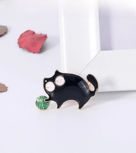 Close-up of a black enamel cat brooch playing with a green ball of yarn jewelry