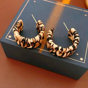 Detail of beige and black woven leopard C-shape earrings on a jewelry box with golden posts
