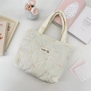 Top view of cream quilted tote bag featuring colorful heart embroidery and logo patch.