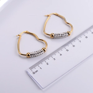 Detail of gold heart earrings with rhinestones next to a ruler for size reference
