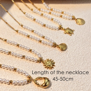 Golden stainless steel necklace with white pearls and marine charms on a soft beige surface