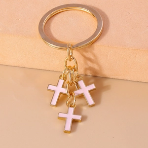 Close-up of golden keychain featuring three pink enamel crosses with polished metal rings