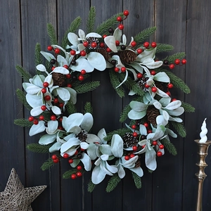 Close-up of Christmas wreath with red berries, pine cones and flocked leaves on dark wood