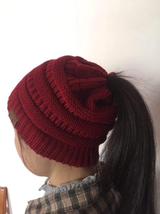 Detail of burgundy ponytail beanie showing thick cable knit texture and top opening