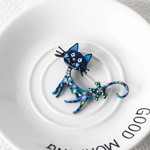 Detail of colorful polka dot enamel cat brooch with pearl and green bow on ceramic plate
