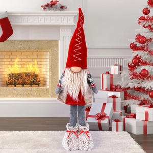 Standing Christmas gnome with red pointed hat and plush boots by fireplace and tree