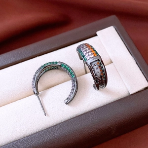 Macro detail of vintage C-shaped earrings with colorful zircons on a brown silk lining