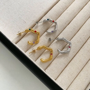 Gold and silver wavy C-shaped earrings with colorful gemstones in a ribbed tray