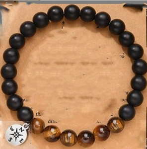 Detail of 8mm matte black and tiger eye bead bracelet with silver compass charm