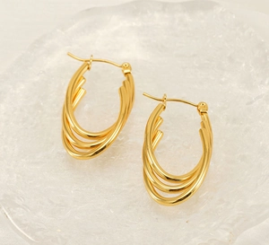 Close-up of 18k gold triple-layered oval hoop earrings on a textured glass tray