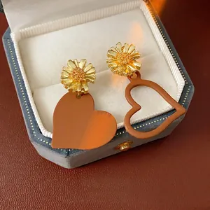 Asymmetric daisy heart dangle earrings in orange and gold finish on velvet box