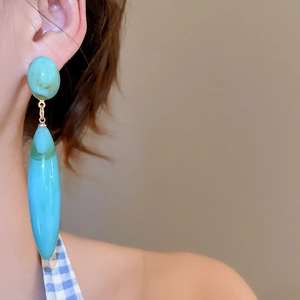 Detail shot of large turquoise acrylic teardrop earrings with a glossy marble texture finish