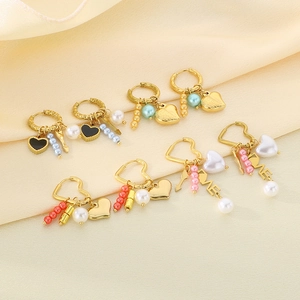 Detail of gold earrings with heart charms and colorful pearls on silk fabric