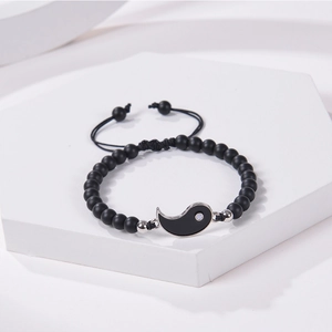 Detail of matte black beads bracelet with Yin Yang charm on white geometric block