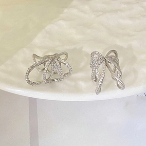 Macro view of silver bow-knot ear cuff with white zircon stones on a ceramic plate