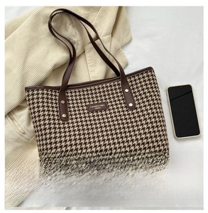 Detail of houndstooth tote bag with leather handles and decorative brand logo tag