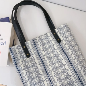 Close-up of floral cotton tote bag with leather handles and gold rivet reinforcements