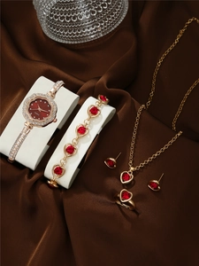 Close-up of gold quartz watch and jewelry set with red heart gems on brown silk fabric
