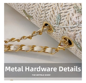 Detail of woven straw bag showing green floral embroidery and light gold metal chain