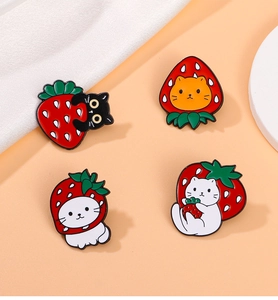 Detailed view of four strawberry cat enamel pins set against a soft pink background