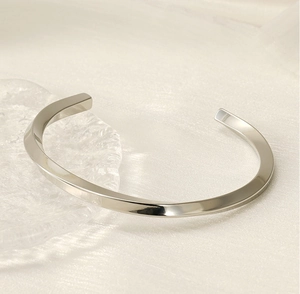 Detailed close-up of a silver C-shaped twisted metal cuff bracelet on silk fabric