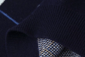 Macro view of navy blue diamond pattern sweater showing fine knit texture and ribbed cuffs