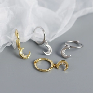 Macro shot of silver and gold crescent moon earrings with cubic zirconia on white silk