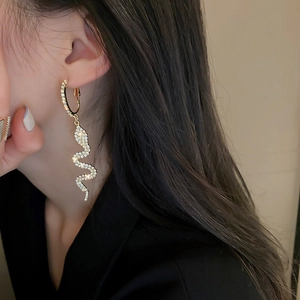 Macro view of gold snake earrings with sparkling rhinestones worn by a model