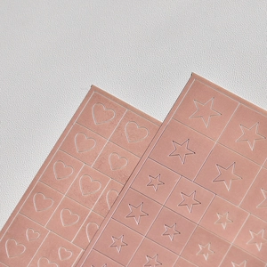 Macro detail of heart and star shaped matte beige skin-tone nail art stickers