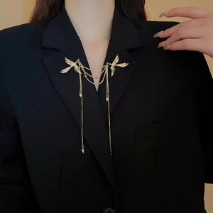 Dettaglio della spilla a fenice dorata con catene a nappa e perle su un blazer nero