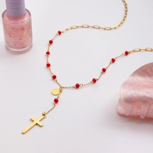 Close-up of gold cross pendant necklace with red beads on a minimalist white background