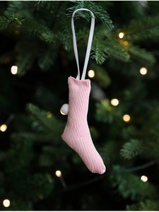 Pink corduroy Christmas stocking ornament with white pompom hanging on a pine tree