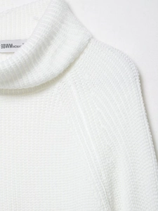 Detailed close-up of white turtleneck knit sweater neckline with woven brand label