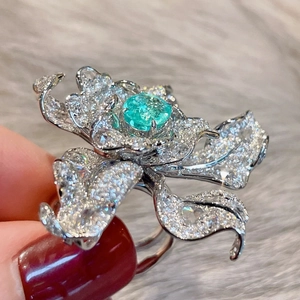 Detailed close-up of a silver flower ring with emerald gemstone and sparkling pavé diamonds
