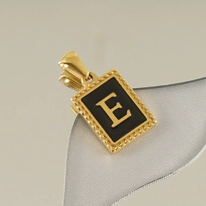 Detail of a gold stainless steel rectangle pendant with black enamel and gold letter E
