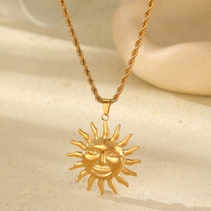 Close-up of gold plated sun god pendant with twisted chain on a minimalist stone base