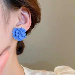 Detail of blue resin floral stud earring featuring layered petals on female model's ear