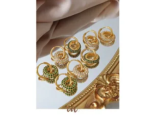Macro shot of gold hoop earrings with white and green crystals on silk backdrop