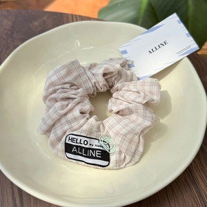 Detail of pink plaid scrunchie featuring a black woven label and mint green paperclip