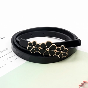 Detail of thin black leather belt featuring three golden floral buckles on light green background