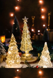 Three glowing glass Christmas trees with warm LED lights on a wooden snow base