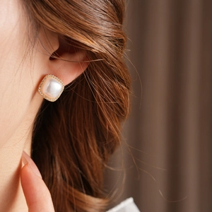 Macro shot of gold plated square stud earring featuring a central pearl and zircon halo