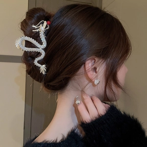 Detailed side view of a golden dragon hair claw with white rhinestones and a red bead