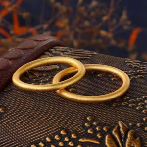 Close-up detail of matte gold plain rings resting on a decorative vintage textured box