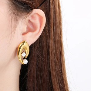 Detailed close-up of a 18K gold teardrop earring with square zircon and white pearl inlay