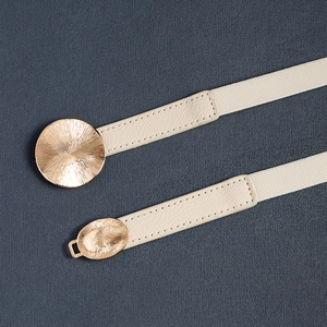 Detail of beige elastic belt with golden metal buckle featuring sunburst texture