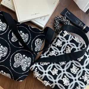 Close-up of canvas shoulder bags with white butterfly embroidery on dark wood surface
