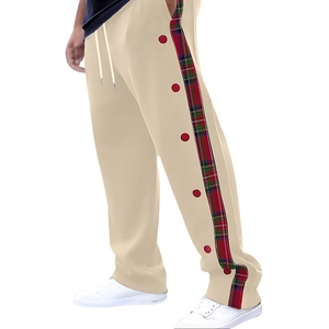 Detail of beige trousers featuring side plaid panel, red buttons, and white drawstring