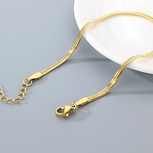 Detail of gold snake chain bracelet with adjustable lobster clasp on white ceramic