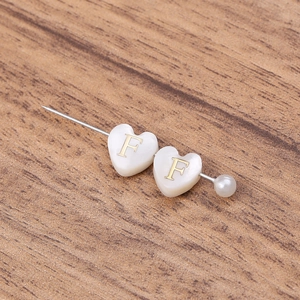 Gros plan sur broche cœur en nacre avec lettre F dorée et détail de perle élégante